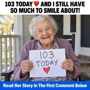 Smiling elderly woman holding a handwritten 103 TODAY birthday sign on her porch